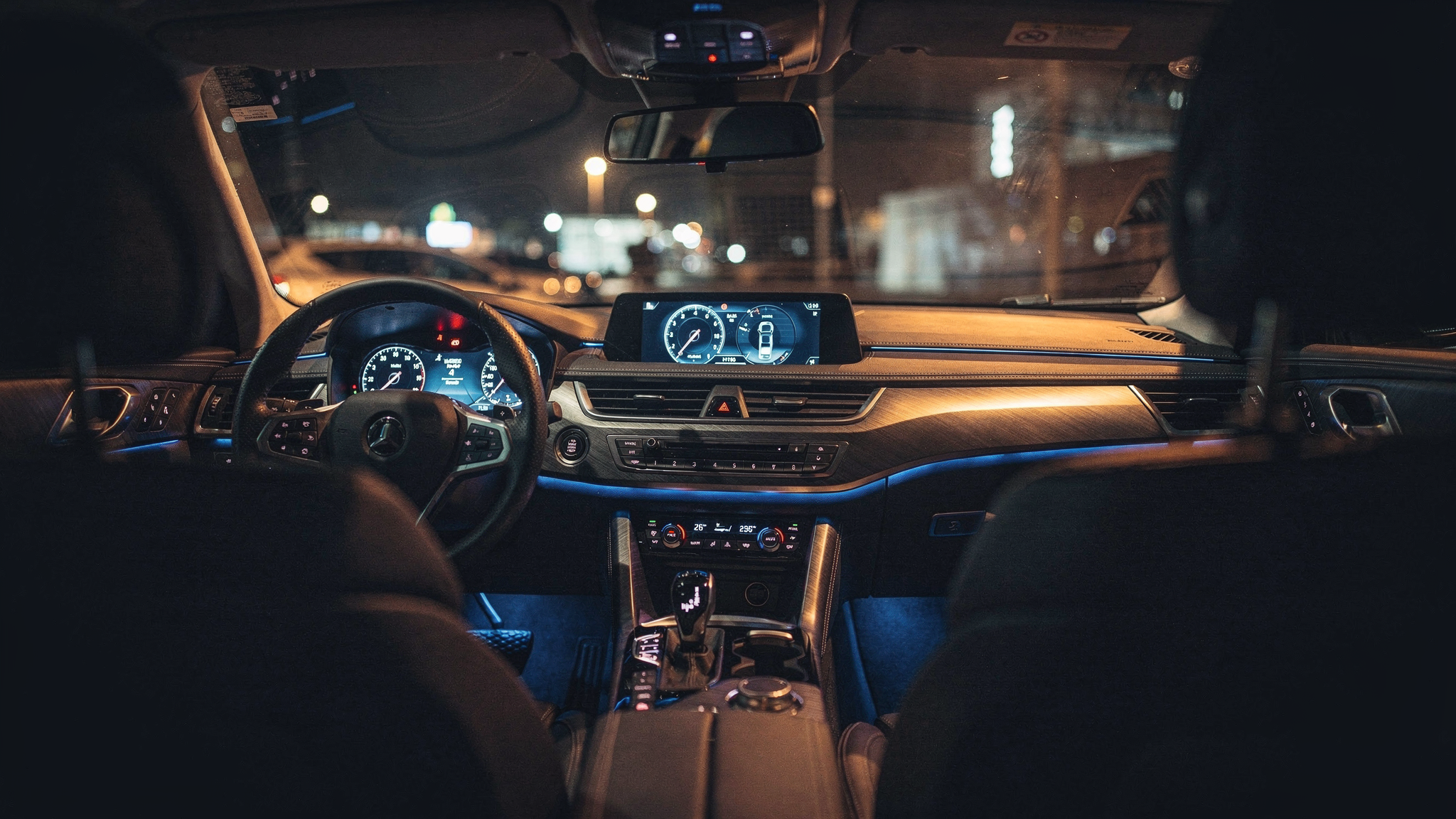 A car cabin interior at night with dashboard glow on glass and metal surfaces